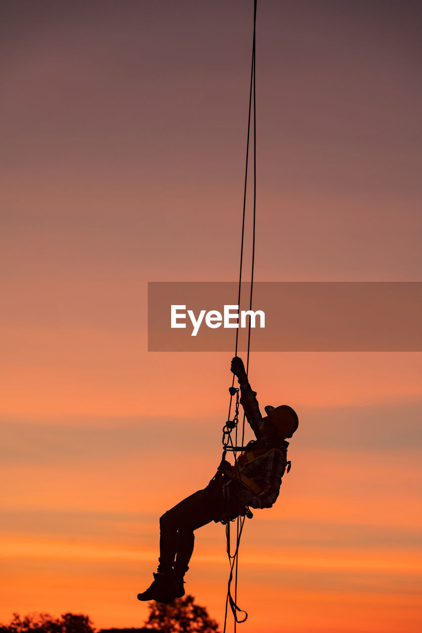 SILHOUETTE MAN WITH ROPE AGAINST SKY AT SUNSET