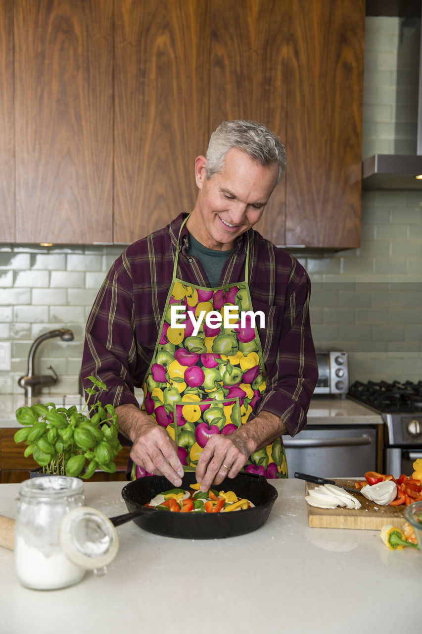 Smiling mature man preparing pizza in kitchen at home