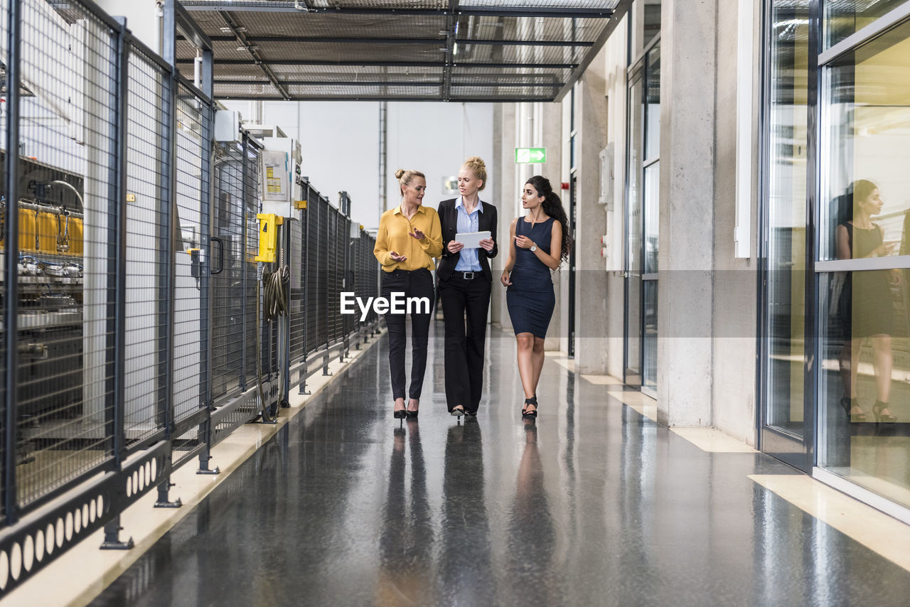 Three women with tablet walking and talking in factory shop floor