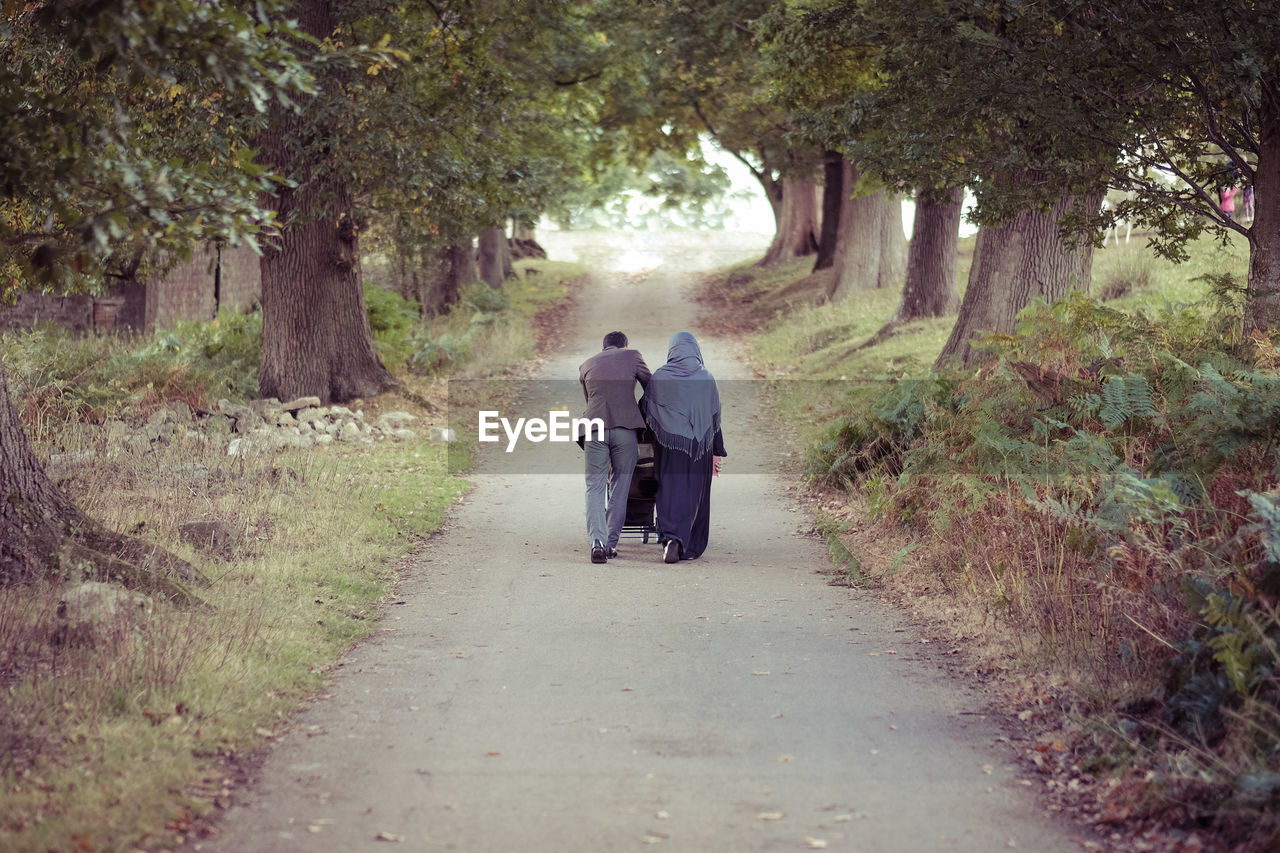 Rear view of man and woman walking on road amidst trees at park