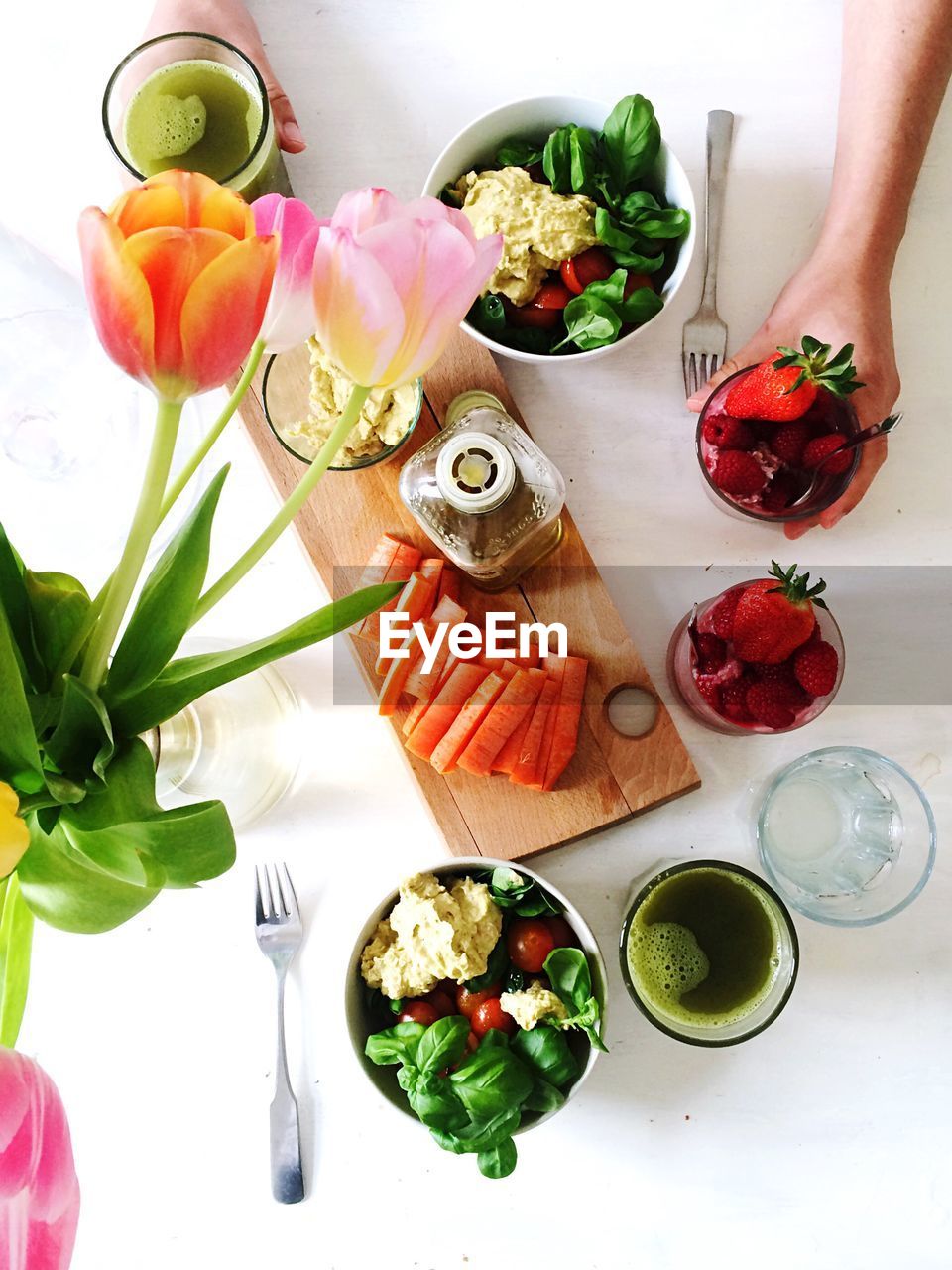 Cropped hands of person holding strawberries in glass by food and tulips at table
