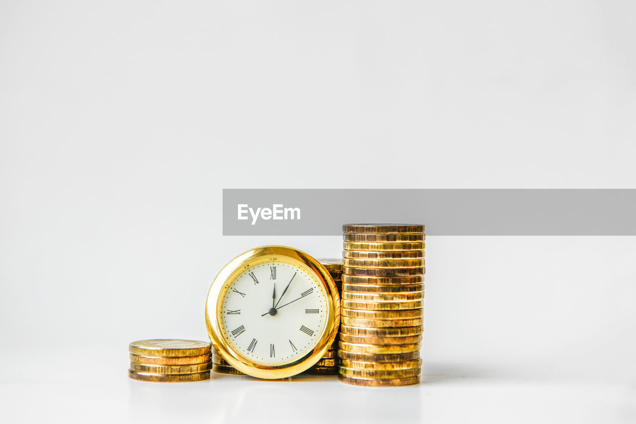 Close-up of coins and clock against white background