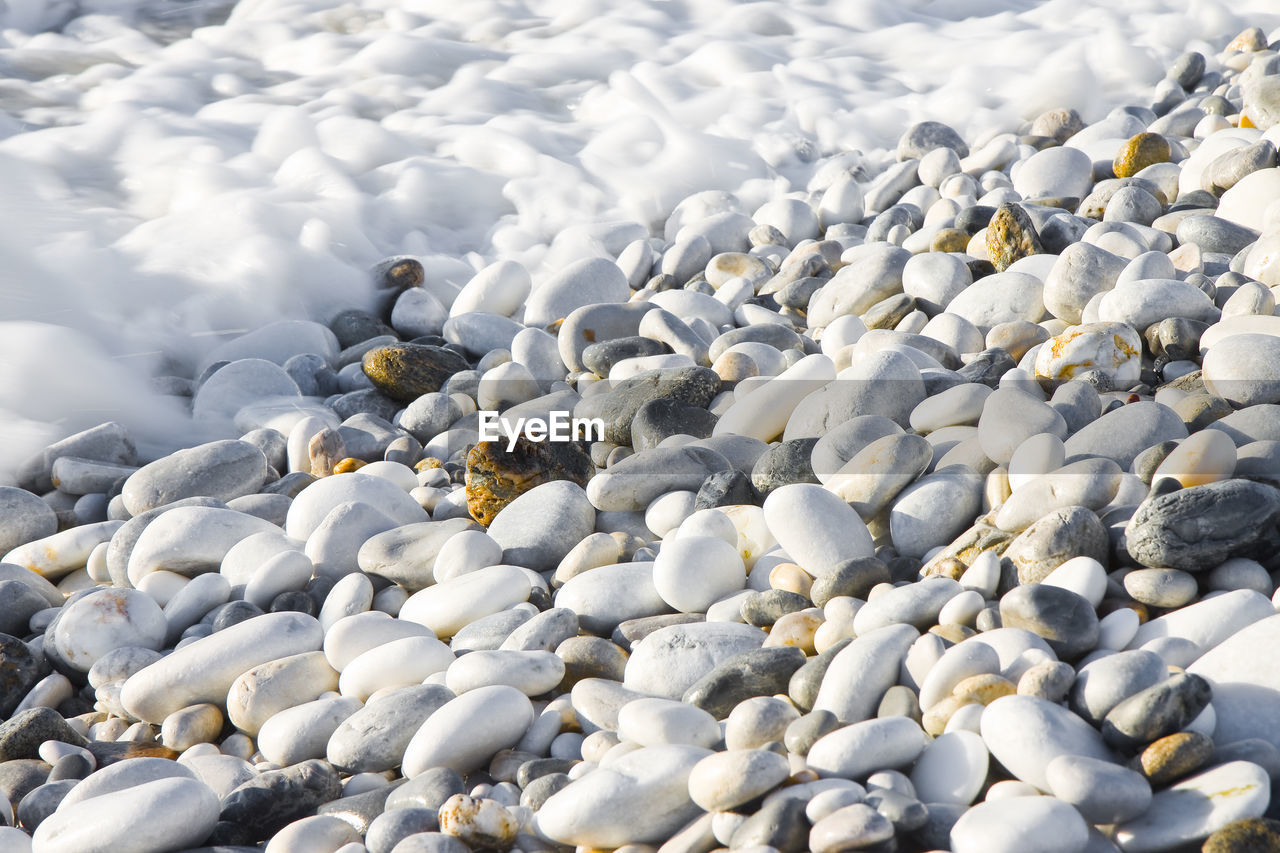 HIGH ANGLE VIEW OF PEBBLES ON SHORE