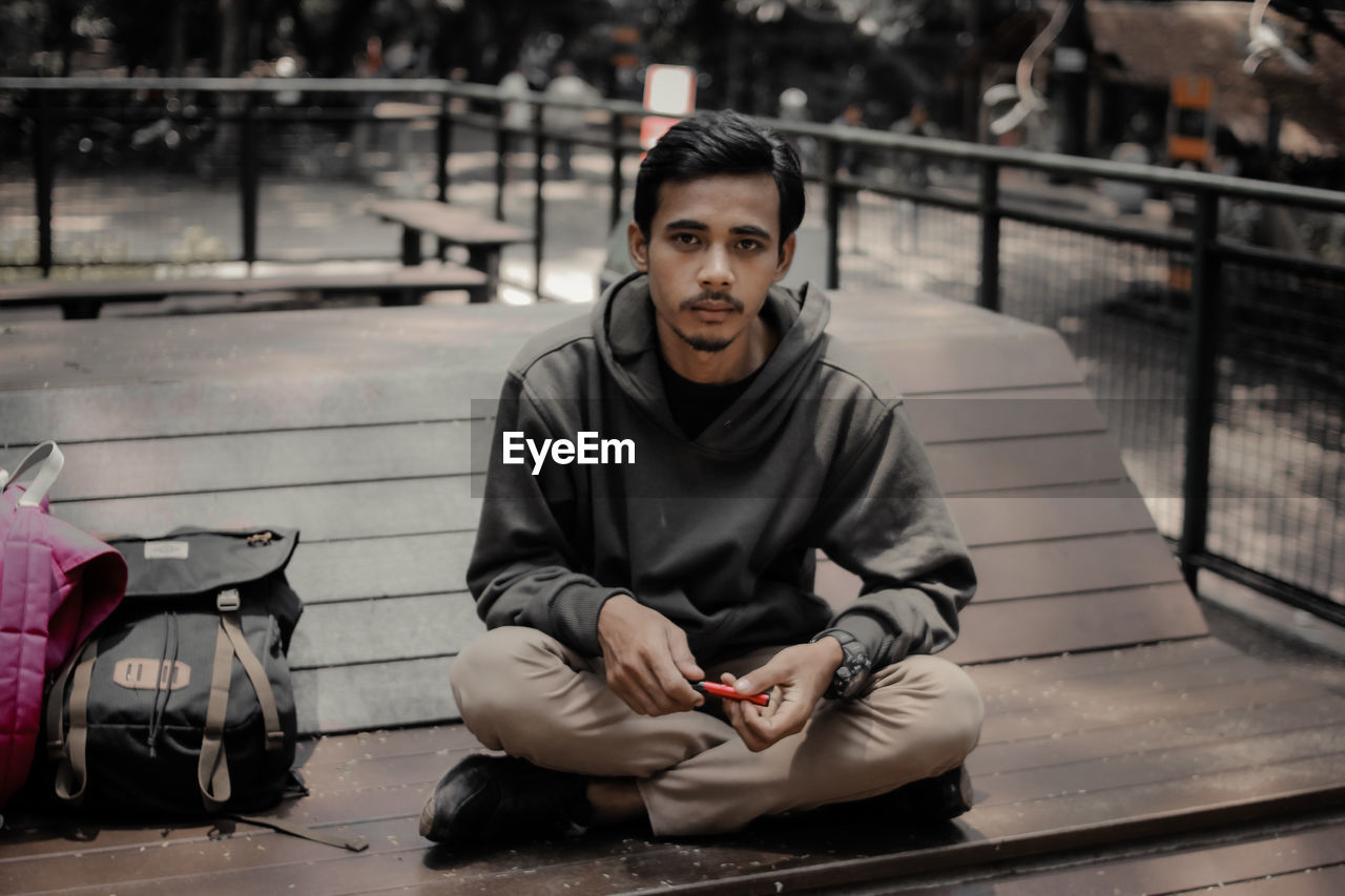 Portrait of young man sitting on railing