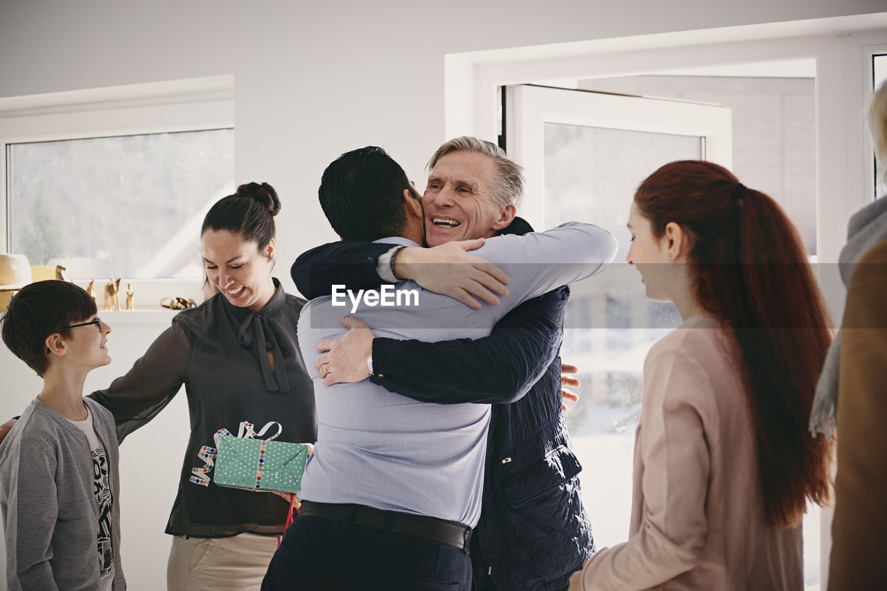 Smiling senior father embracing man while standing by family at doorway