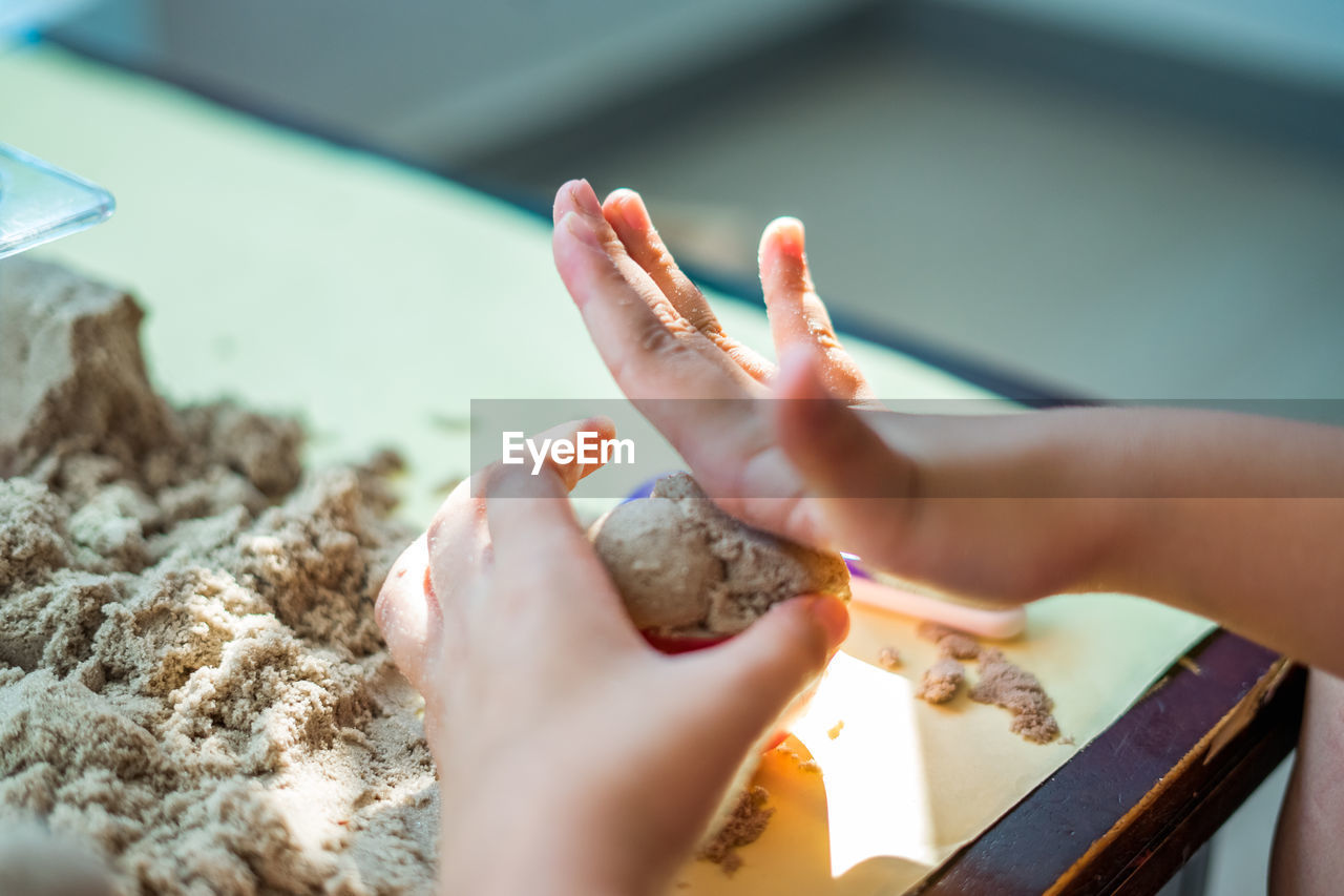 Cropped hand of child playing with sand on table