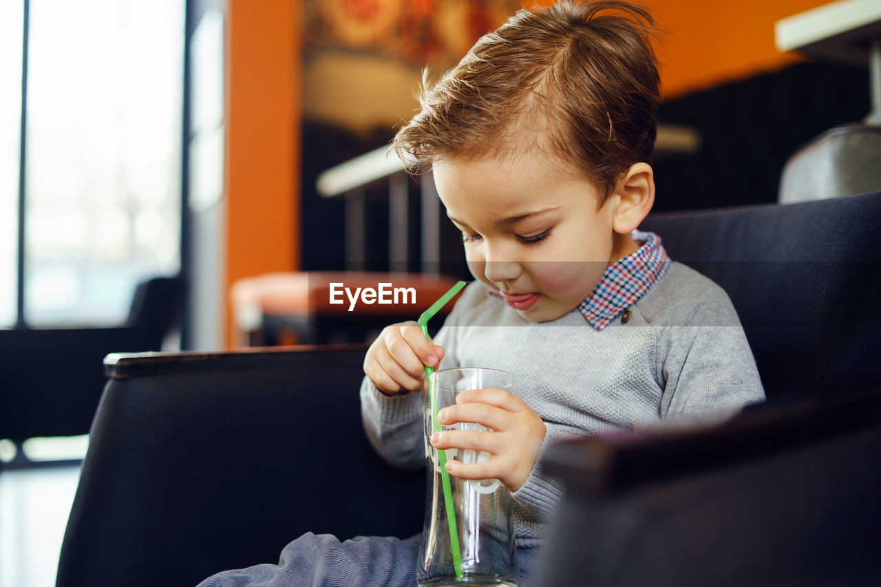 Cute boy holding drinking glass sitting on sofa at home