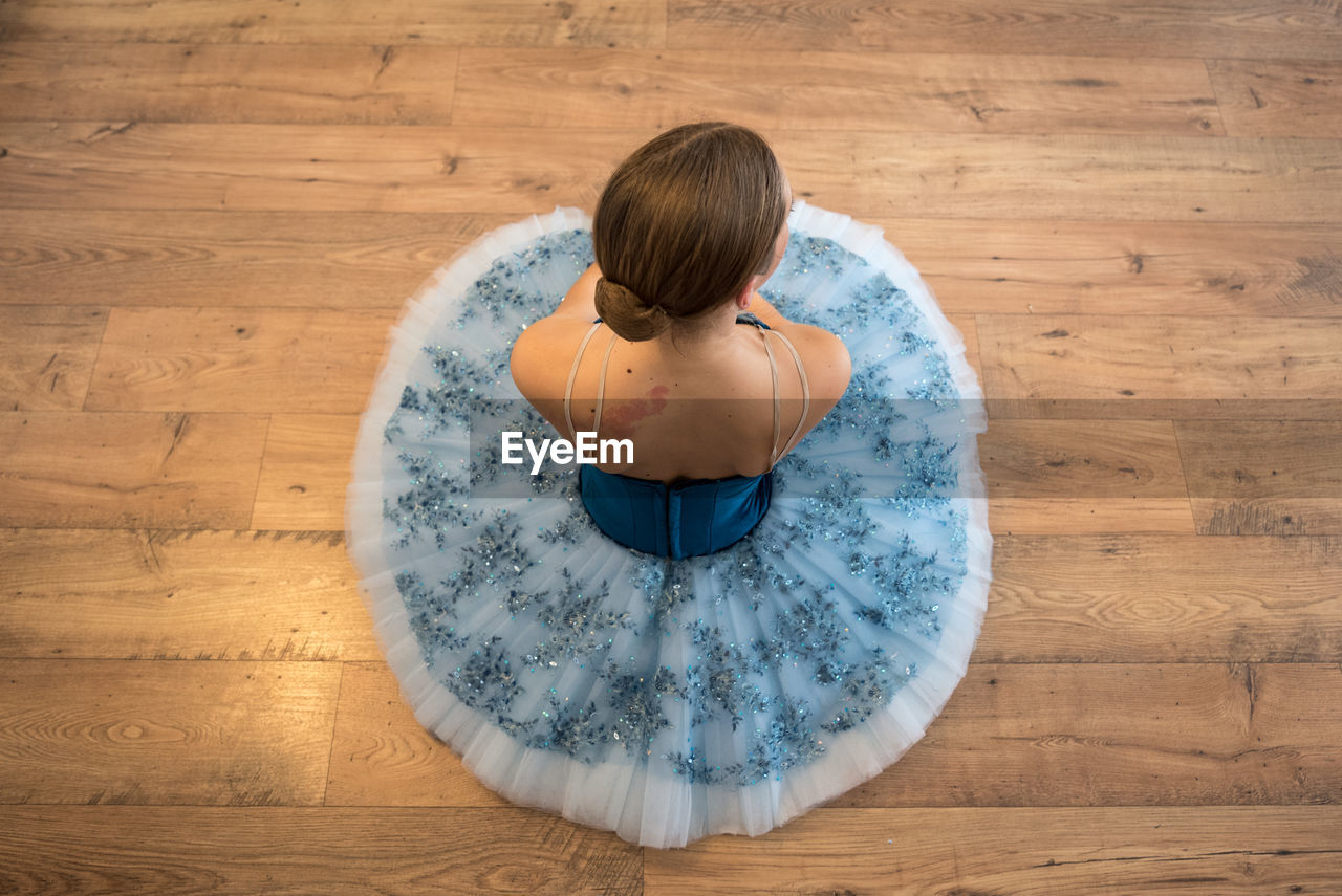 REAR VIEW OF WOMAN SITTING ON HARDWOOD FLOOR IN SUNLIGHT