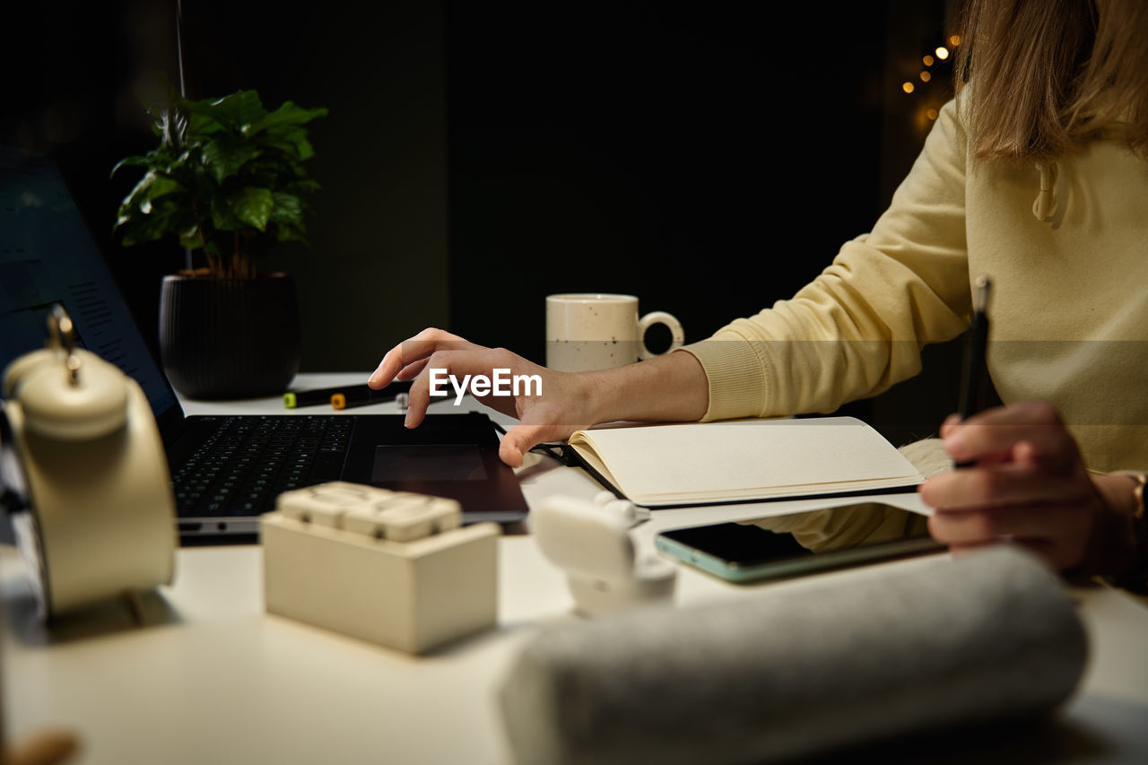 Woman working from home workplace at night, using laptop