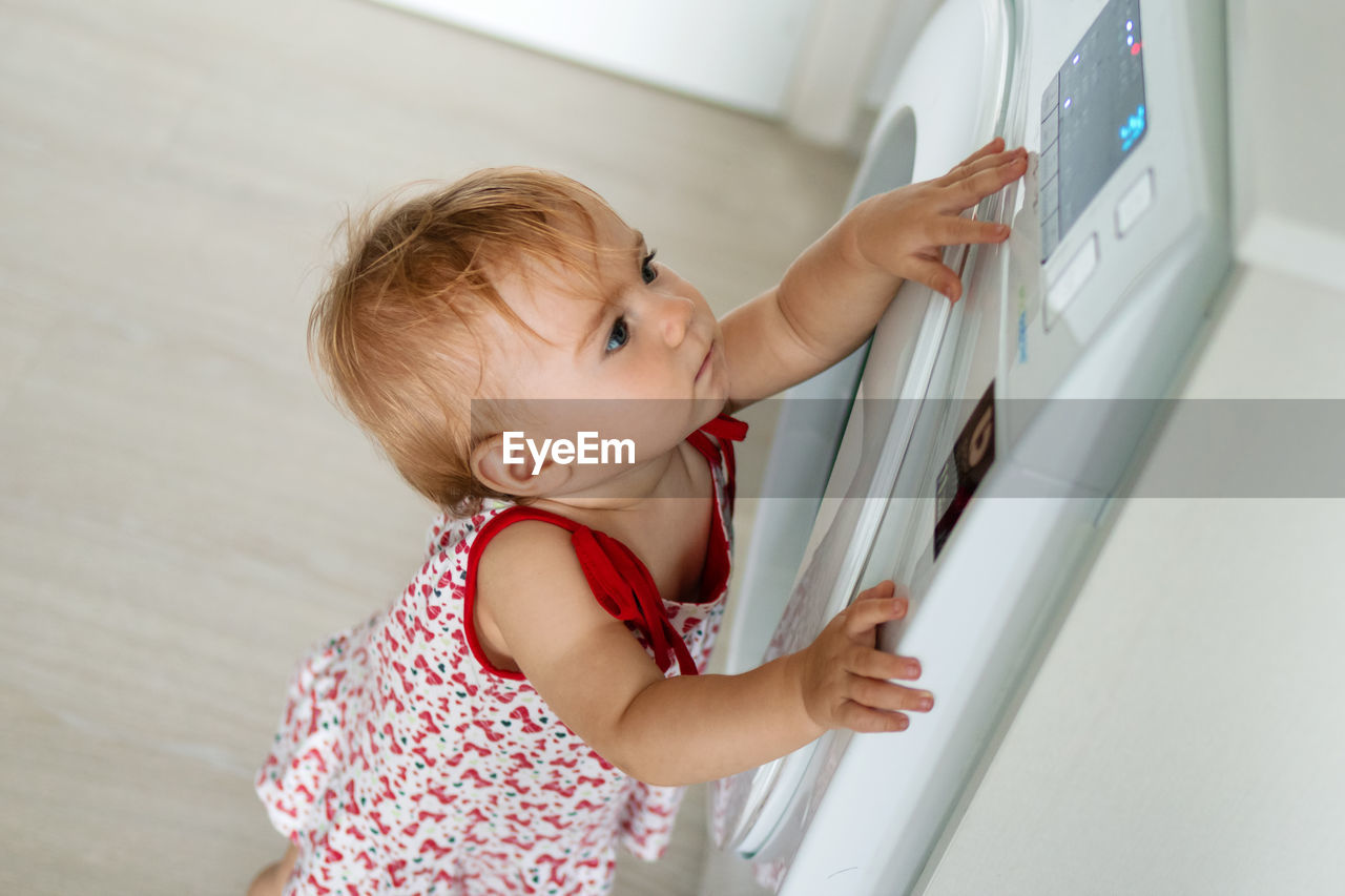 Side view of cute girl standing by washing machine