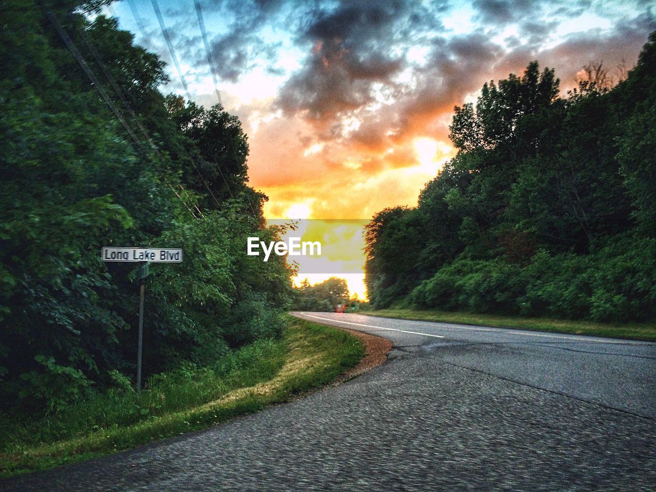 ROAD PASSING THROUGH FOREST AGAINST CLOUDY SKY