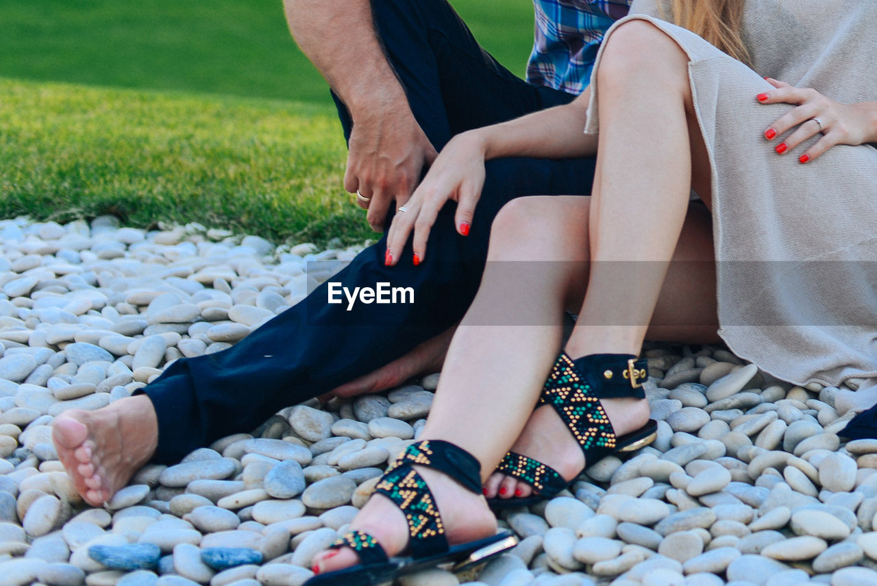 Low section of man and woman sitting by pebbles