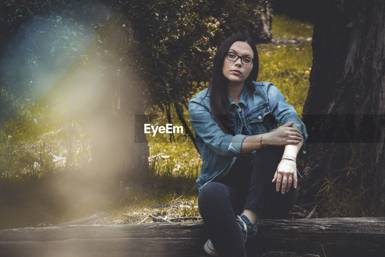 Portrait of young woman sitting on tree trunk in forest