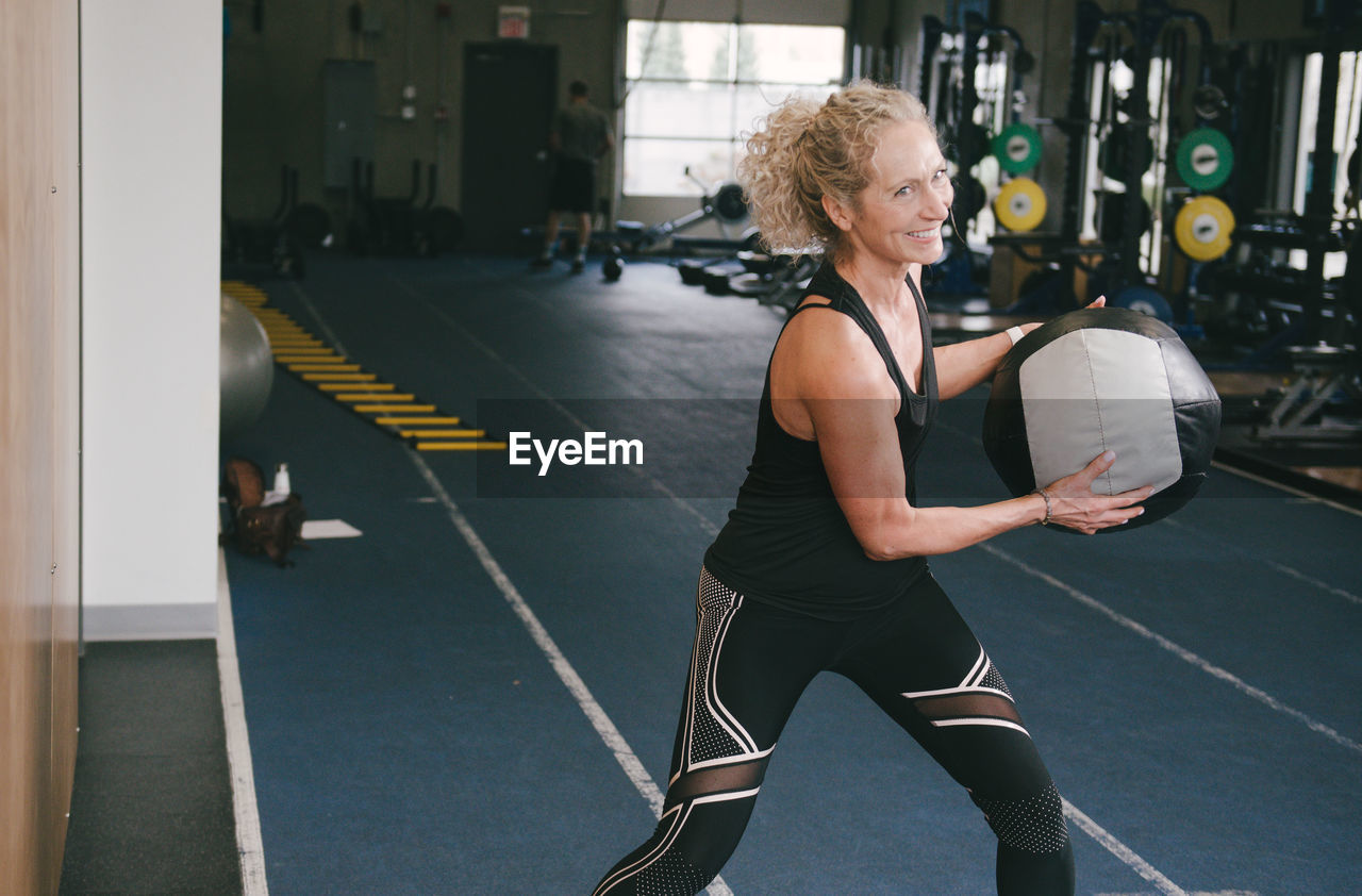 Smiling woman exercising with medicine ball while at gym