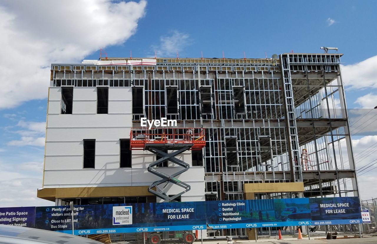 LOW ANGLE VIEW OF CRANE AGAINST BUILDING AGAINST SKY