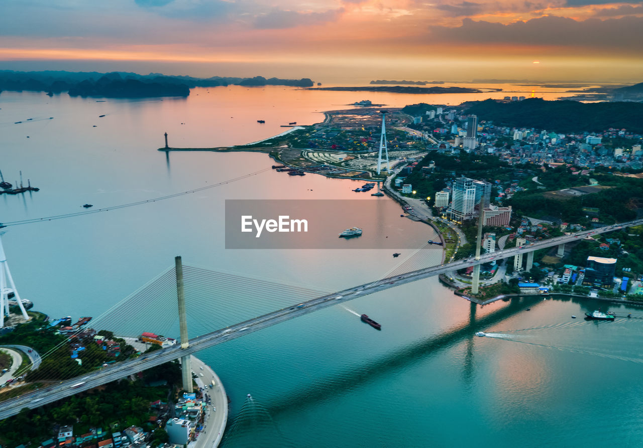 Aerial view of bridge over bay in city during sunset