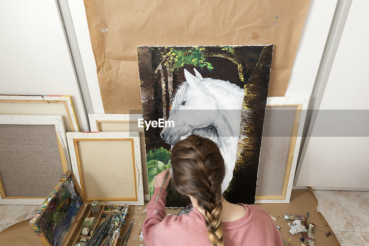 High angle view of teenage girl painting horse on canvas at home