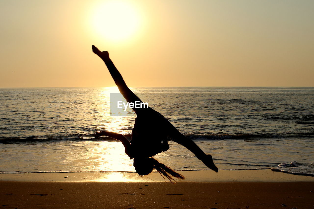 Silhouette woman jumping on sand at beach during sunset