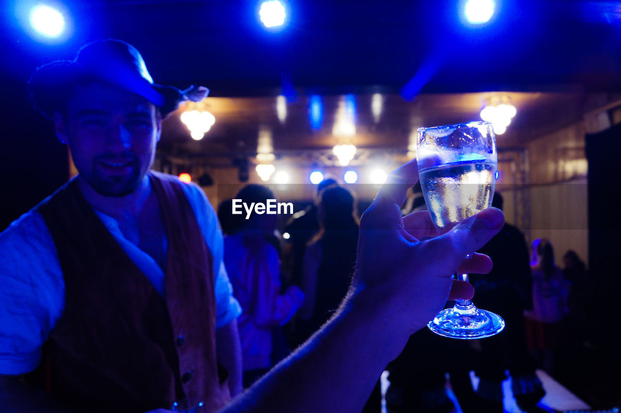 Cropped image of hand holding wineglass with friends during party in background