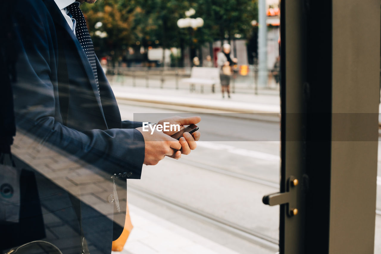 Midsection of mature businessman using smart phone seen from glass door