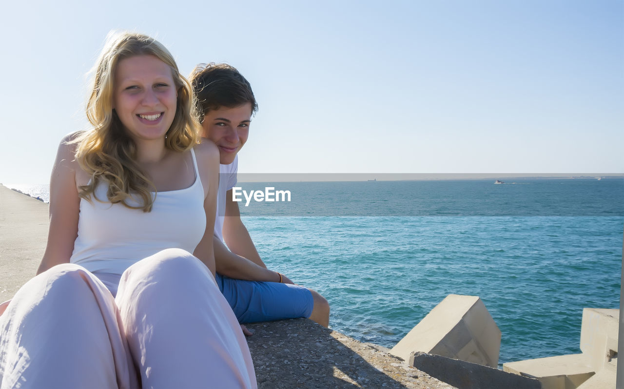 portrait of young woman sitting against sea against clear sky