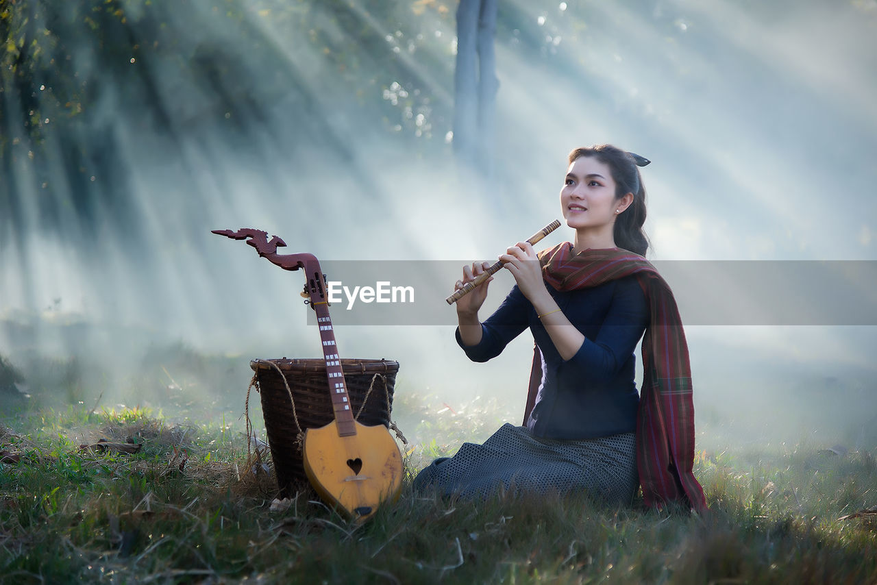 Beautiful woman playing flute while sitting at park