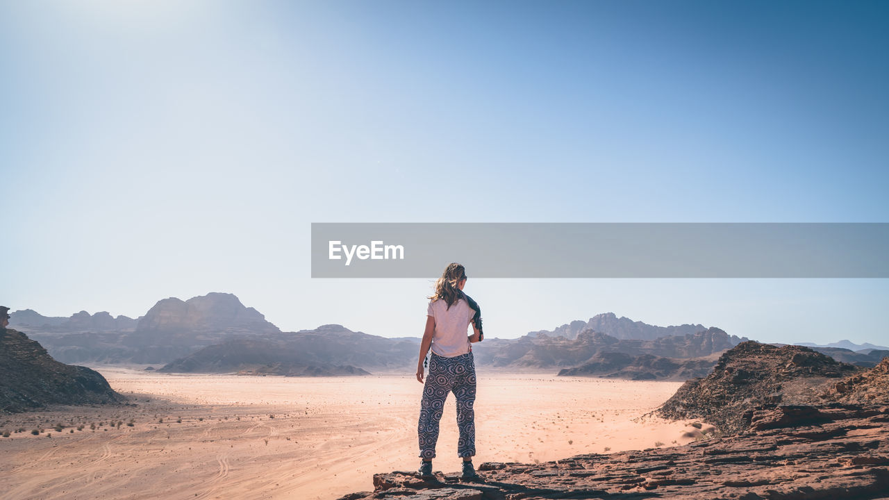 Rear view of woman standing on cliff by landscape against clear sky