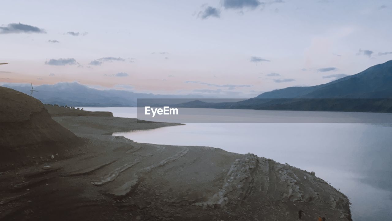 SCENIC VIEW OF LAKE BY MOUNTAINS AGAINST SKY DURING SUNSET