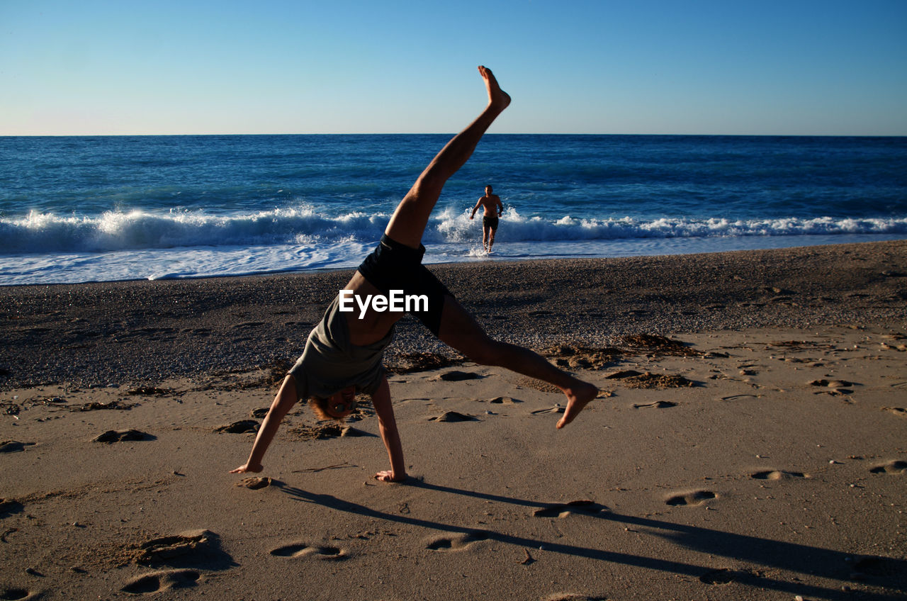 Full length of young men exercising at beach