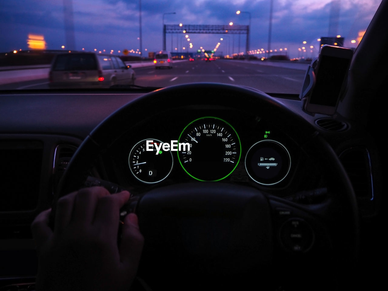 Cropped hand driving car on bridge at dusk