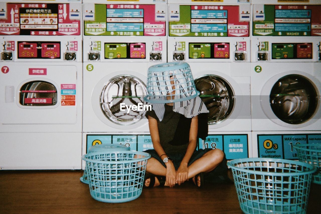 Young woman wearing laundry basket in laundromat