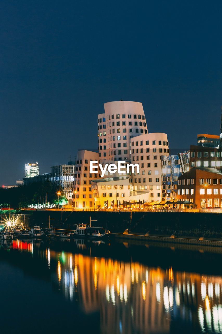 Illuminated buildings by river against sky at night