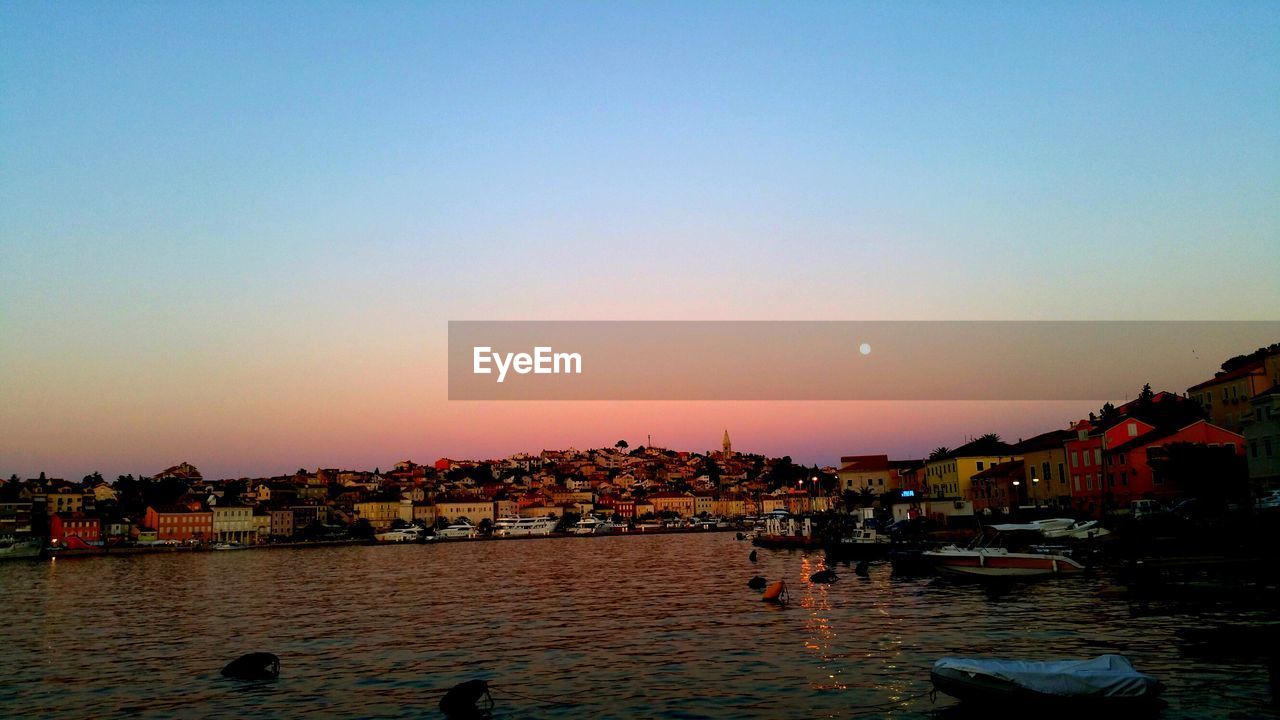 Buildings in front of river against clear sky at dusk