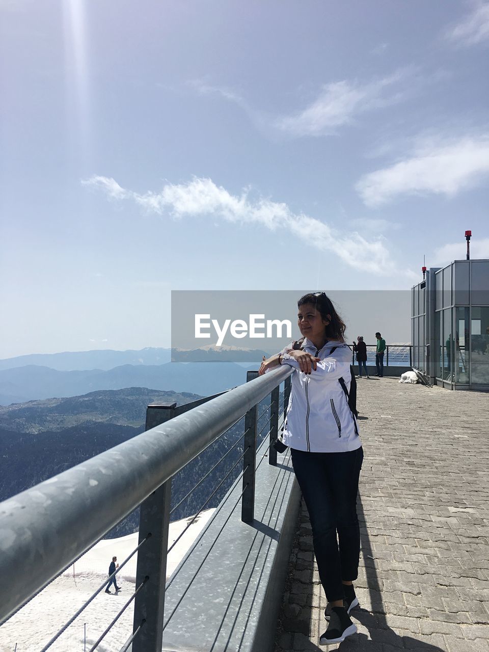 Full length of woman looking at view while standing by railing against blue sky during sunny day