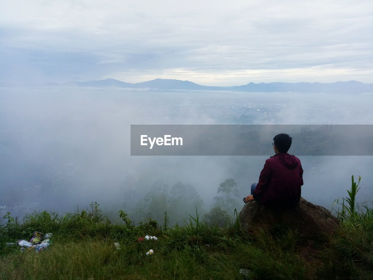 Rear view of man sitting on mountain against sky