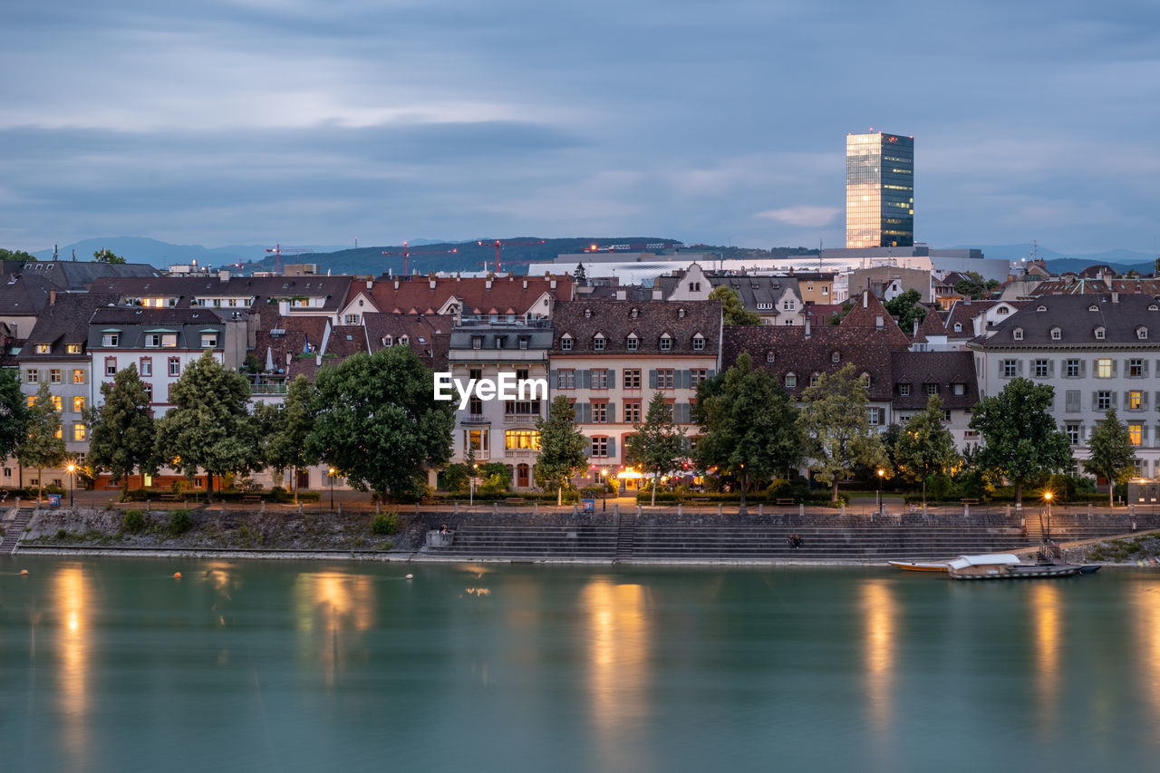 Buildings by river against sky in city at dusk