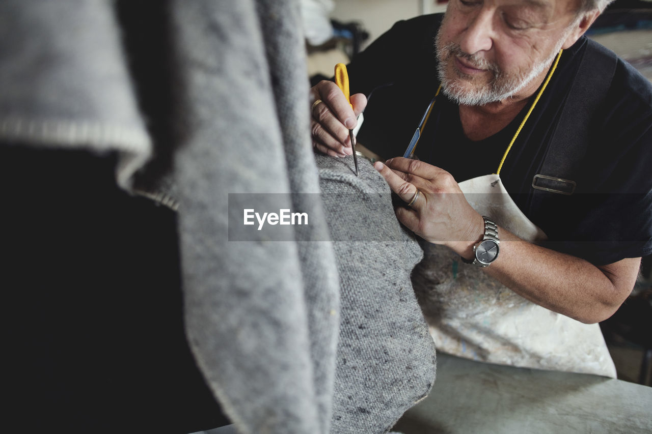 Close-up of senior craftsperson working on gray fabric at workshop