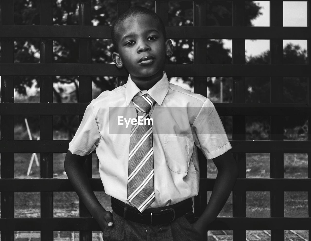 Portrait of boy in school uniform standing against fence