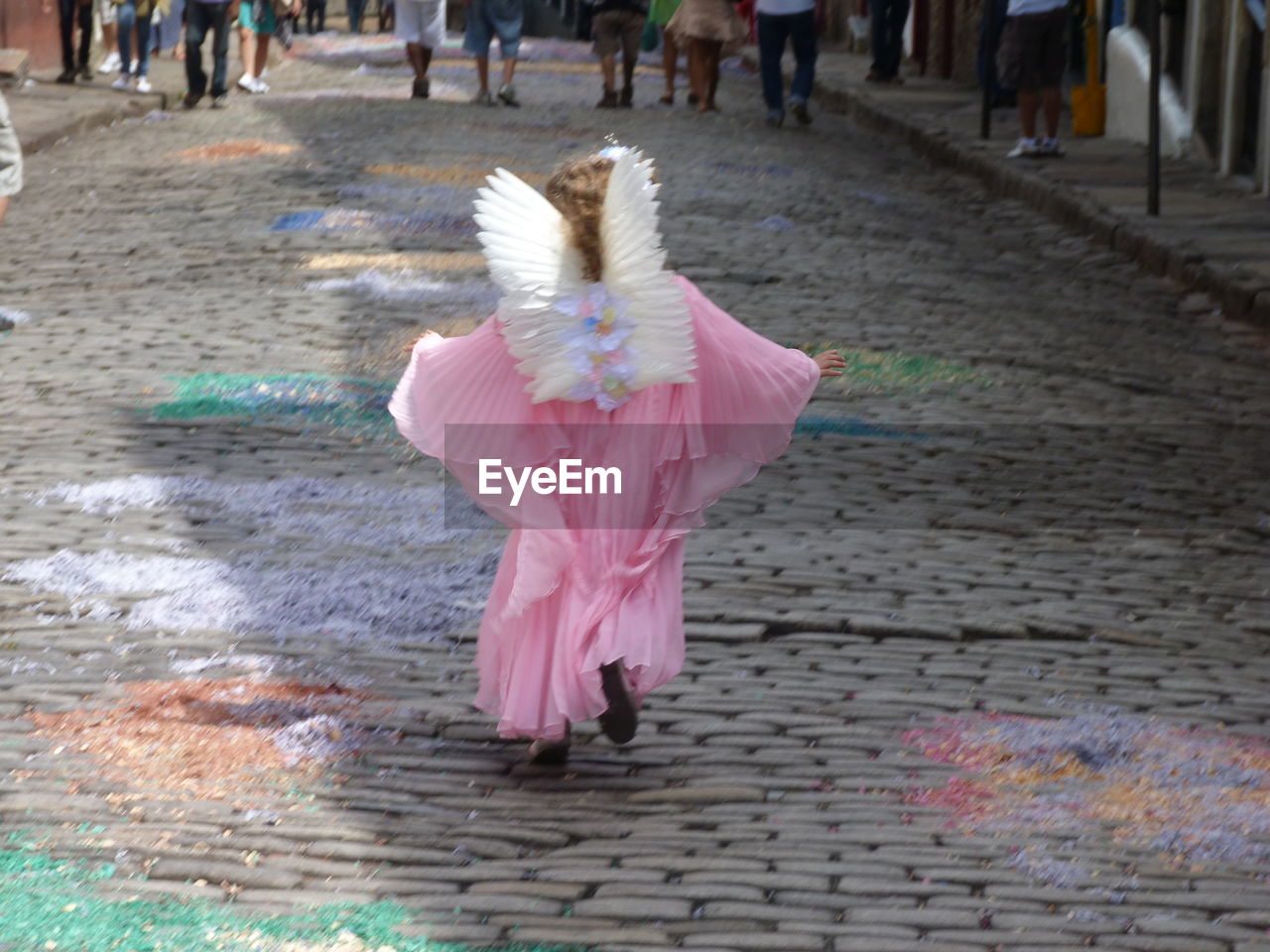 Rear view of girl in angel costume running on street