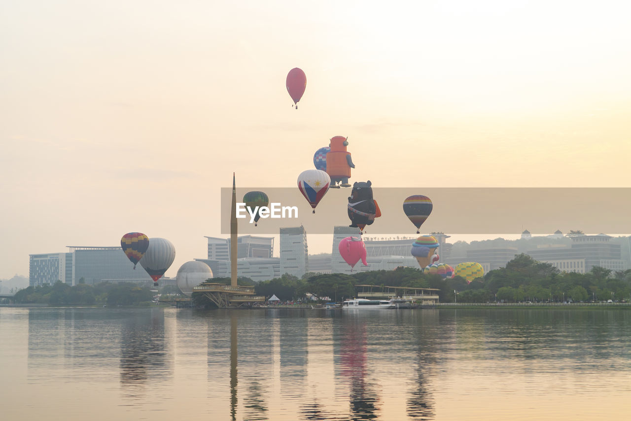 HOT AIR BALLOONS FLYING OVER LAKE AGAINST SKY