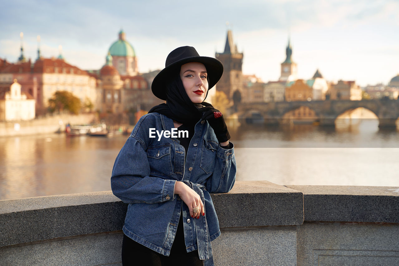 Stylish beautiful young woman earing black hat in prague with charles bridge on background. 