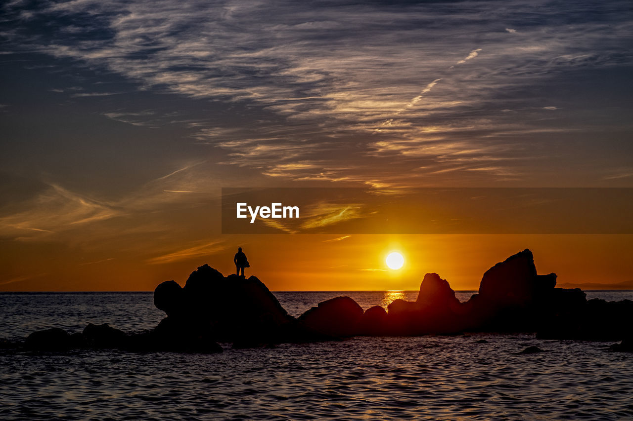 Silhouette rocks on sea against sky during sunset