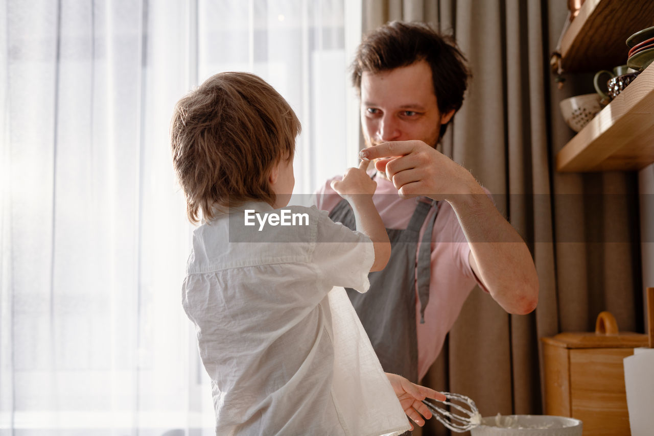 Dad holds a blender and plays with his little son. rubs his nose with whipped cream