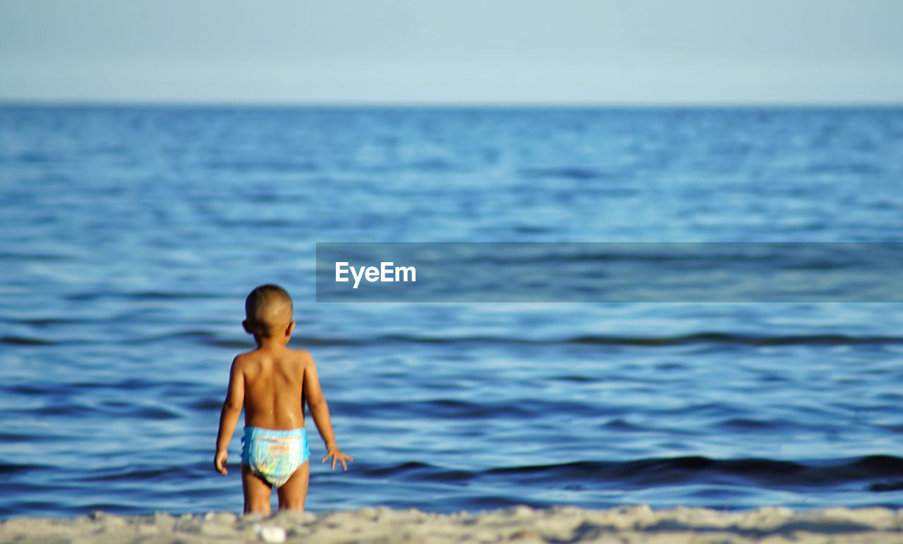 Rear view of shirtless boy standing at beach