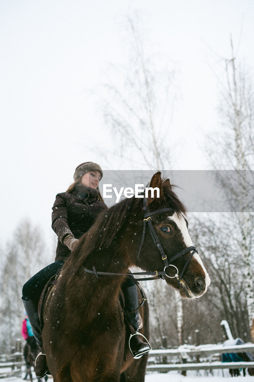 Low angle view of beautiful woman riding horse on snow covered field