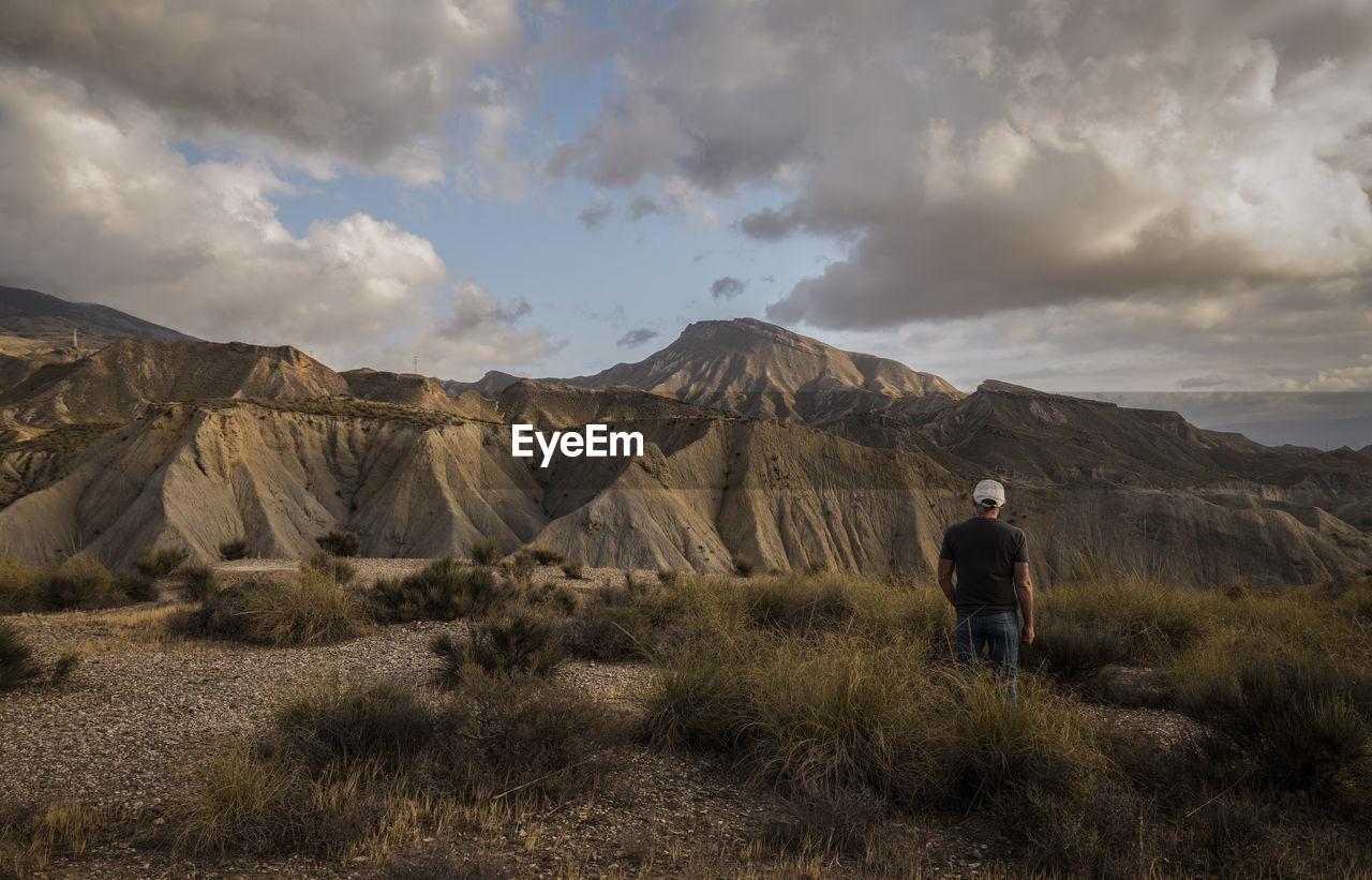 Rear view of man standing on mountain against sky