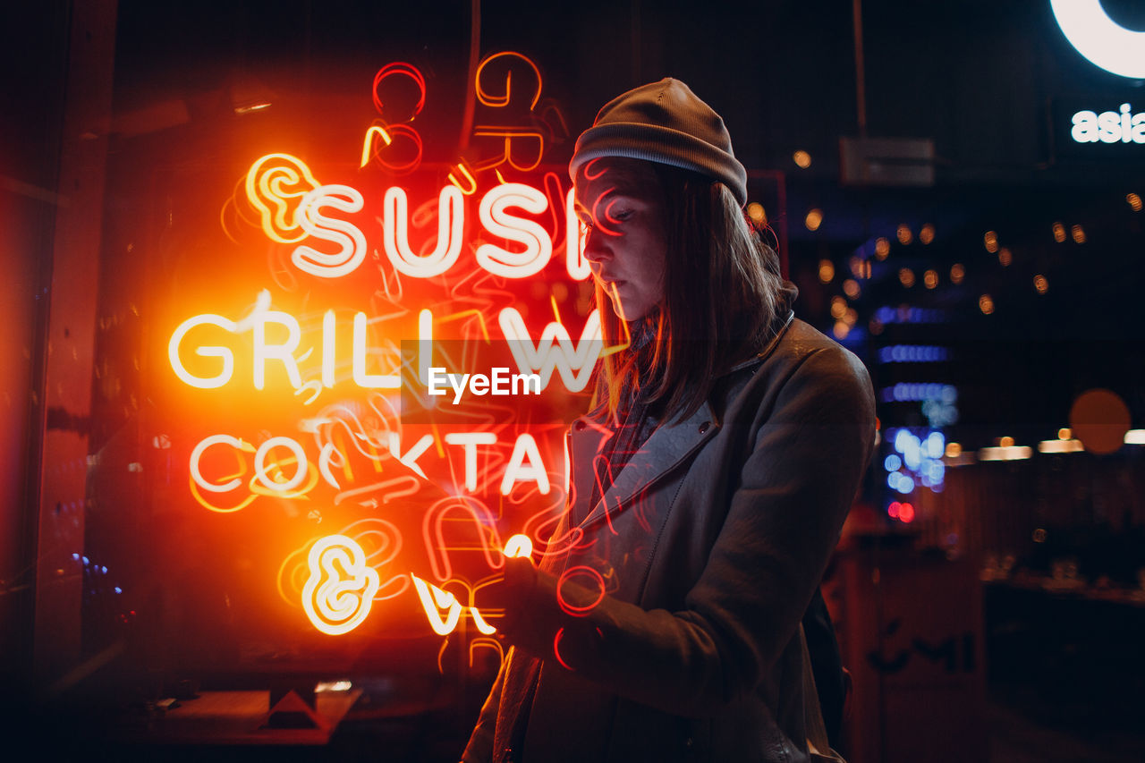 Woman standing by illuminated text at night