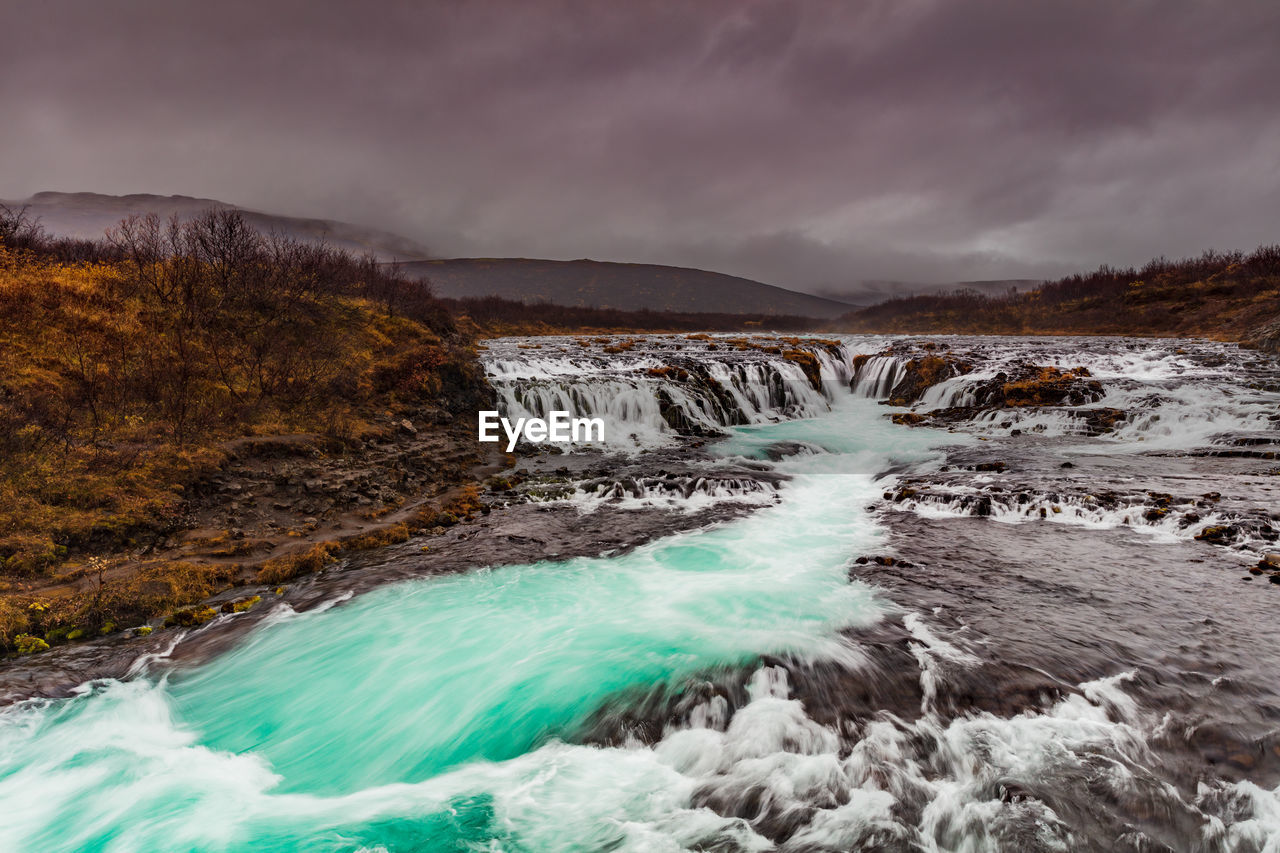 Scenic view of waterfall against cloudy sky