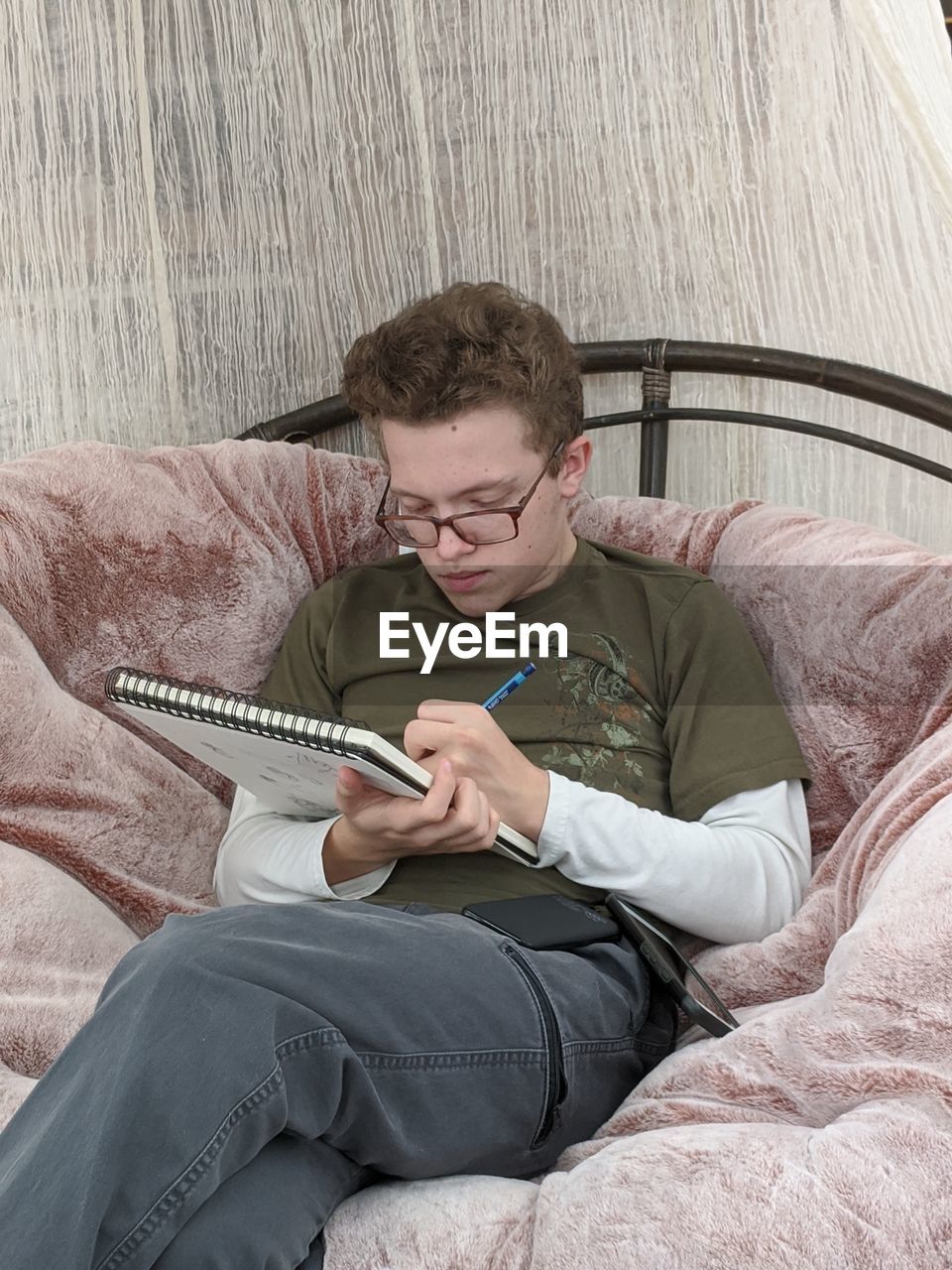 Teenage boy drawing on a sketch pad while sitting in a large chair