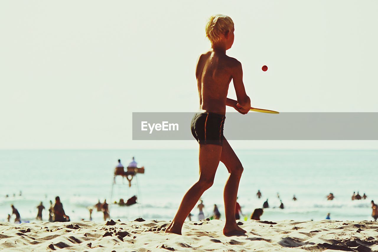 Teenage boy playing on beach against clear sky